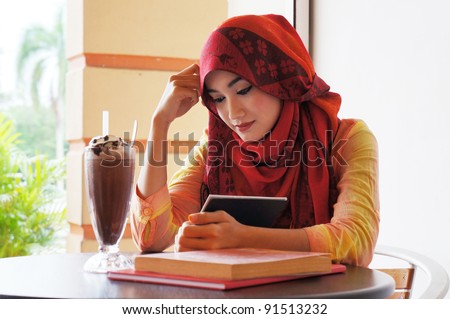 Beautiful muslim woman wearing red scarf  reading at a cafe with books and coffee on the table