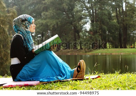 Beautiful muslim woman wearing scarf  with notebook at a lake garden