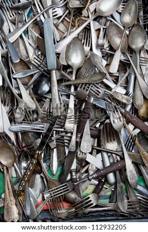 old spoons, teaspoons, knifes and forks in a box on a flea market