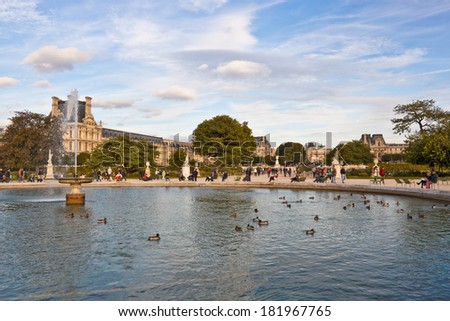 PARIS, FRANCE - SEPTEMBER 19, 2013:  People walking and relaxing in famous green chairs near the fountain in Tuileries Garden - one of the most popular touristic landmarks in Paris.