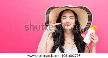 Young woman holding a bottle of sunblock on a solid background