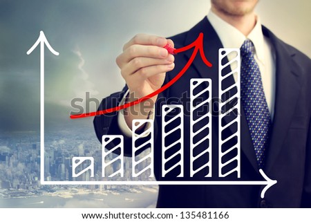 Businessman drawing a rising arrow over a bar graph above the city