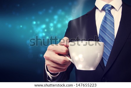 Business man holding a steaming cup of hot coffee on blue modern background