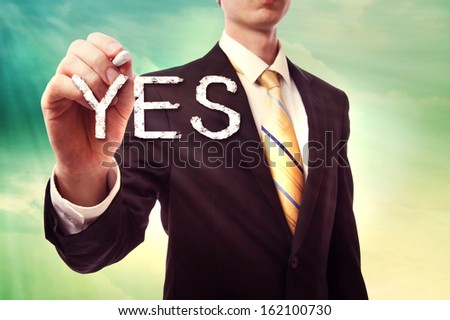 Businessman drawing YES over turquoise yellow colored sky background