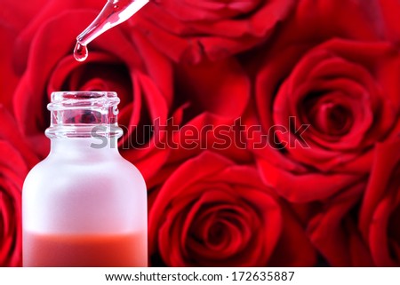 Dropper bottle with rose essence over beautiful red roses