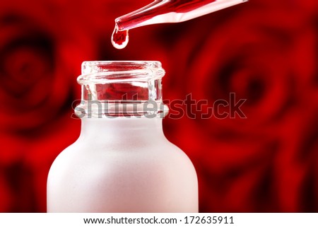 Dropper bottle with rose essence over beautiful red roses