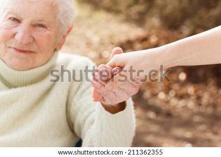 Elderly woman holding hands with young woman outside