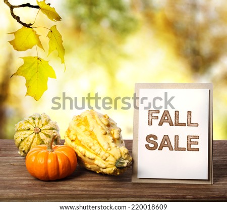 Fall Sale sign on a wooden table with pumpkins on yellow autumn leaves background