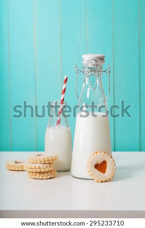 Old fashion milk jars with heart shaped cookies on pastel blue background