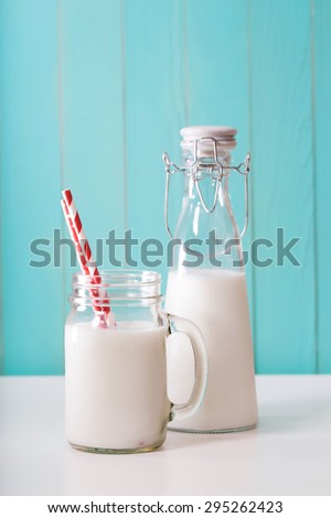 Old fashion milk jar and mason jar with big red paper striped straws on pastel blue background