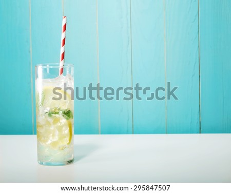 Iced lemonade with big red striped straws on pastel blue background