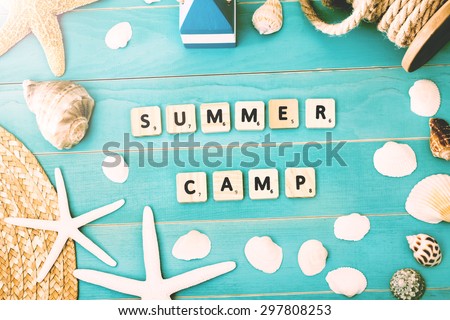 White Scrabble Pieces on Light Blue Table with Assorted Sea Shells and Starfish for Summer Camp Concept