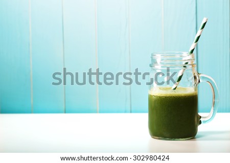 Green smoothie in masons jar with paper straw on blue wooden wall