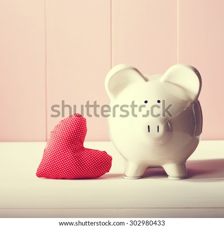 Piggy bank with red heart pillow on pink wooden wall