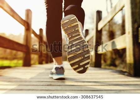 Young woman jogging across an old country bridge at sunset