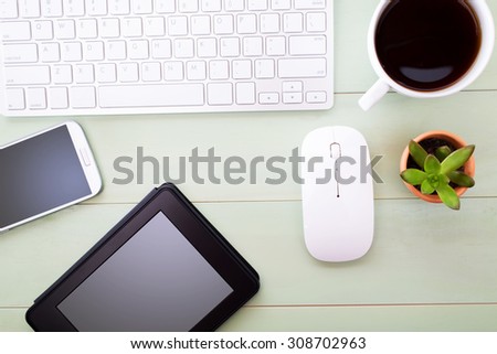 Neat workstation on a wooden desk viewed from overhead with a wireless computer mouse and keyboard, mobile phone, tablet, cup of coffee and houseplant