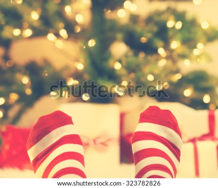 Feet with striped socks with Christmas gift boxes under the tree