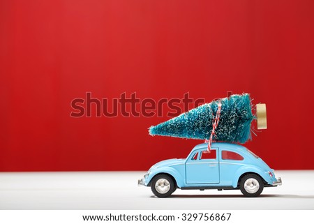 Miniature car carrying a Christmas tree on red colored wooden wall