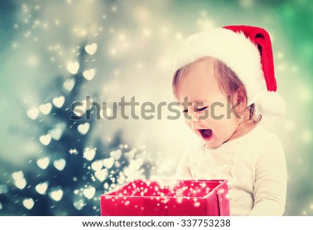 Happy Toddler girl with a Santa hat looking at Christmas present box