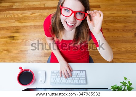 Happy young woman wearing red glasses in her home office