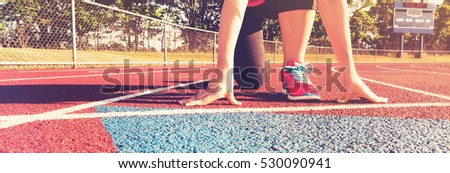 Female athlete on the starting line of a stadium track preparing for a run