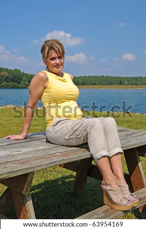 Attractive Middle Aged Woman sitting on picnic table by the Lake