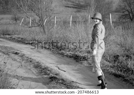 Black and white photography of cheerful young girl walking on a dirt road in rubber boots.