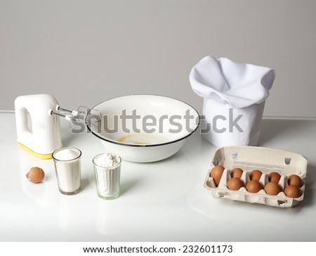 Photo of a cooking still-life with mixer, flour, eggs, sugar, bowl.