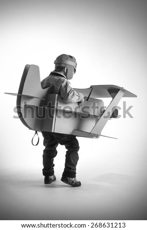 Child is flying away on hand made cardboard plane. Back view. Black and white photo.