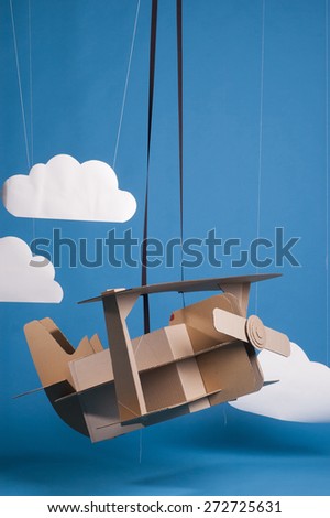 Hand made airplane made of cardboard on blue sky with paper clouds.