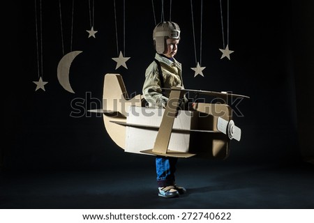 Young pilot is flying on cardboard airplane at night. Side view.