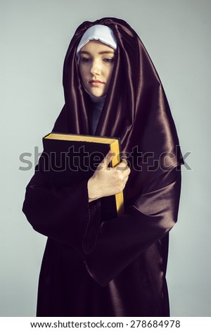 portrait of young woman nun holding bible over gray background.