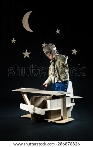 Boy is playing with handmade toy plane. Decorations of night sky is on background.