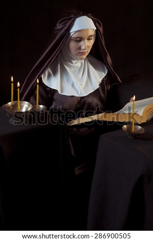 Young beautiful woman nun reading bible on black  background. Through the candles.