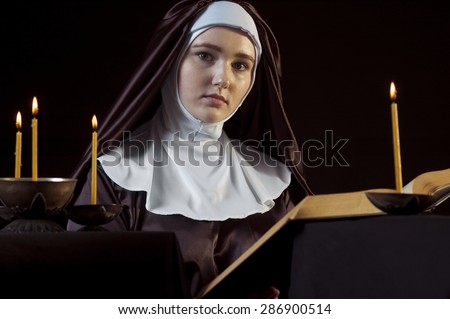 Young beautiful woman nun reading bible on black  background. Through the candles. Low-key lighting.