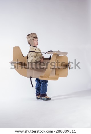 Young pilot is flying on cardboard airplane.  Side view.