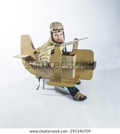 Boy in a pilots costume salutes. The action takes place near the cardboard airplane.