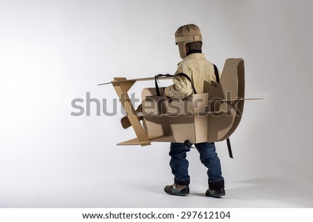 Child is flying away on hand made cardboard plane. Back view.