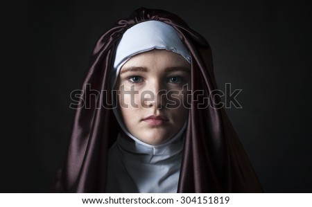Front portrait of the young beautiful nun. Low key lighting. On black.