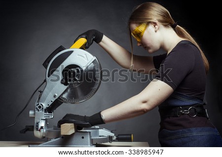 young beautiful woman in overalls and glasses with disk saw preparing for cutting. Photo on black background.