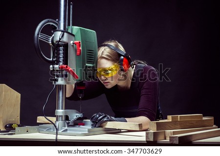 beautiful female carpenter at work using vertical drilling machine. Photo on black background.