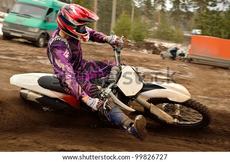 Motocross athlete under helm with a raised leg executes a right turn, on a sand track