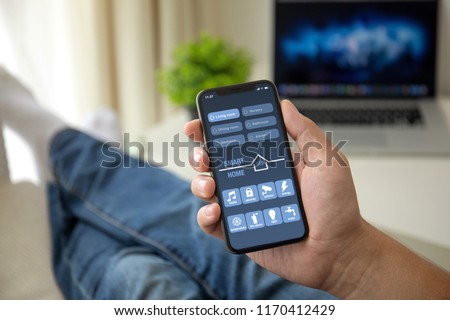 man on sofa holding phone with app smart home on screen in room house