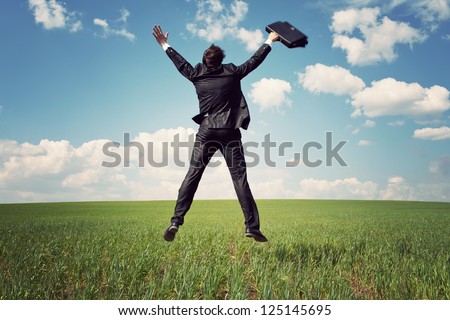 businessman in suit jumping in field and holding the bag