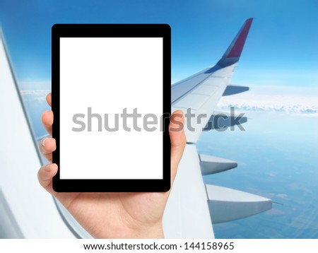 man hand holding a tablet computer with isolated screen against the background of the window with blue sky and airplane wing