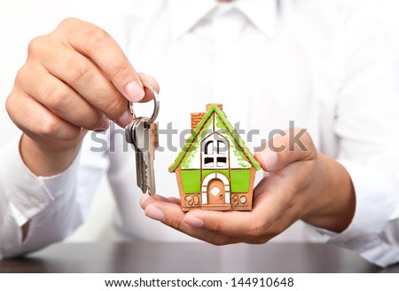 businessman in white shirt holding a small house and apartment keys in hand