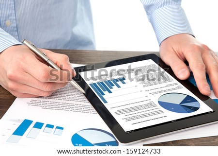 businessman holding a tablet computer with graphics on a screen on the table with documents