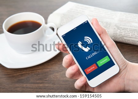 businesswoman hand holding a phone with blue screen and the phone ringing tube against the background of the table in the office