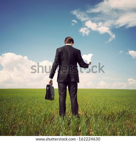 businessman in a suit standing on a green field with a blue sky and reads the newspaper or documents