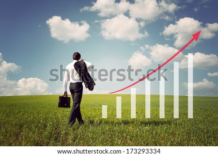 businessman with briefcase in the field with green grass and blue sky rises on the chart with red arrow up